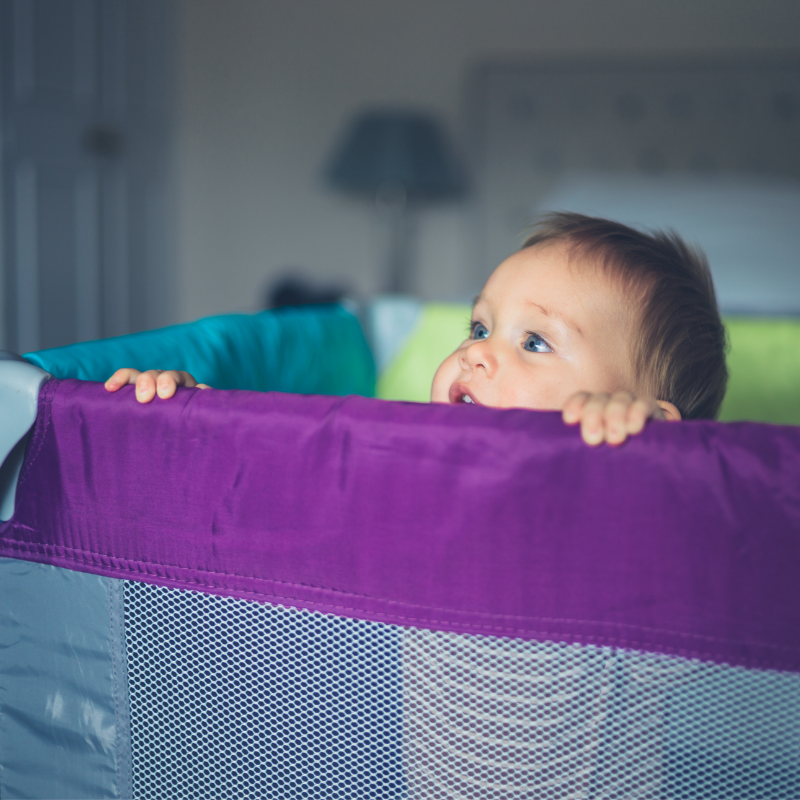 Baby peering over the top of a temporary cot - night nannies can help settle active nighttime children!